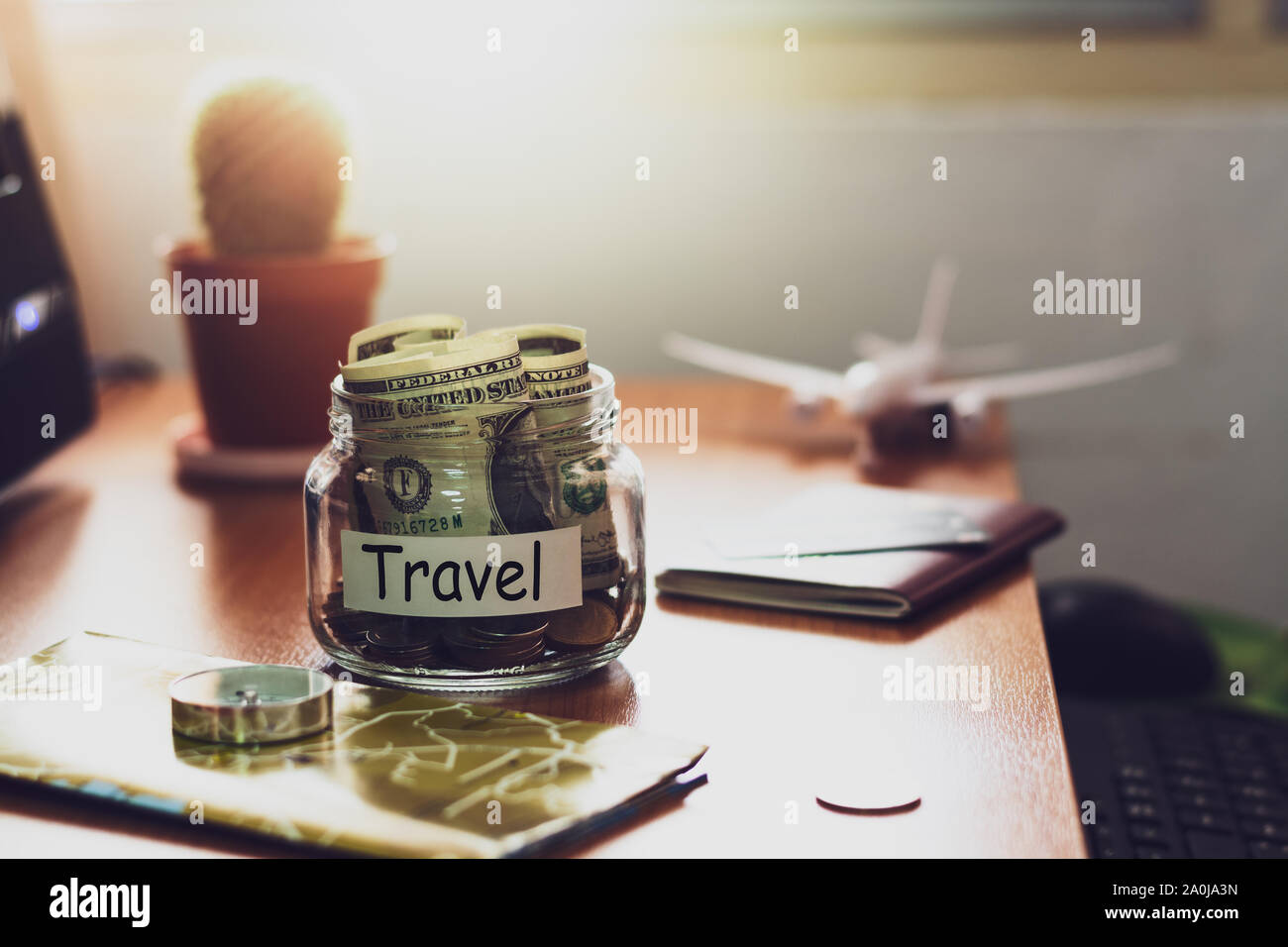 Budget di viaggio concetto. I soldi per il viaggio risparmi in un vasetto di vetro con bussola, passaporto e carta di credito, aereo giocattolo e mappa del mondo sulla scrivania. Foto Stock