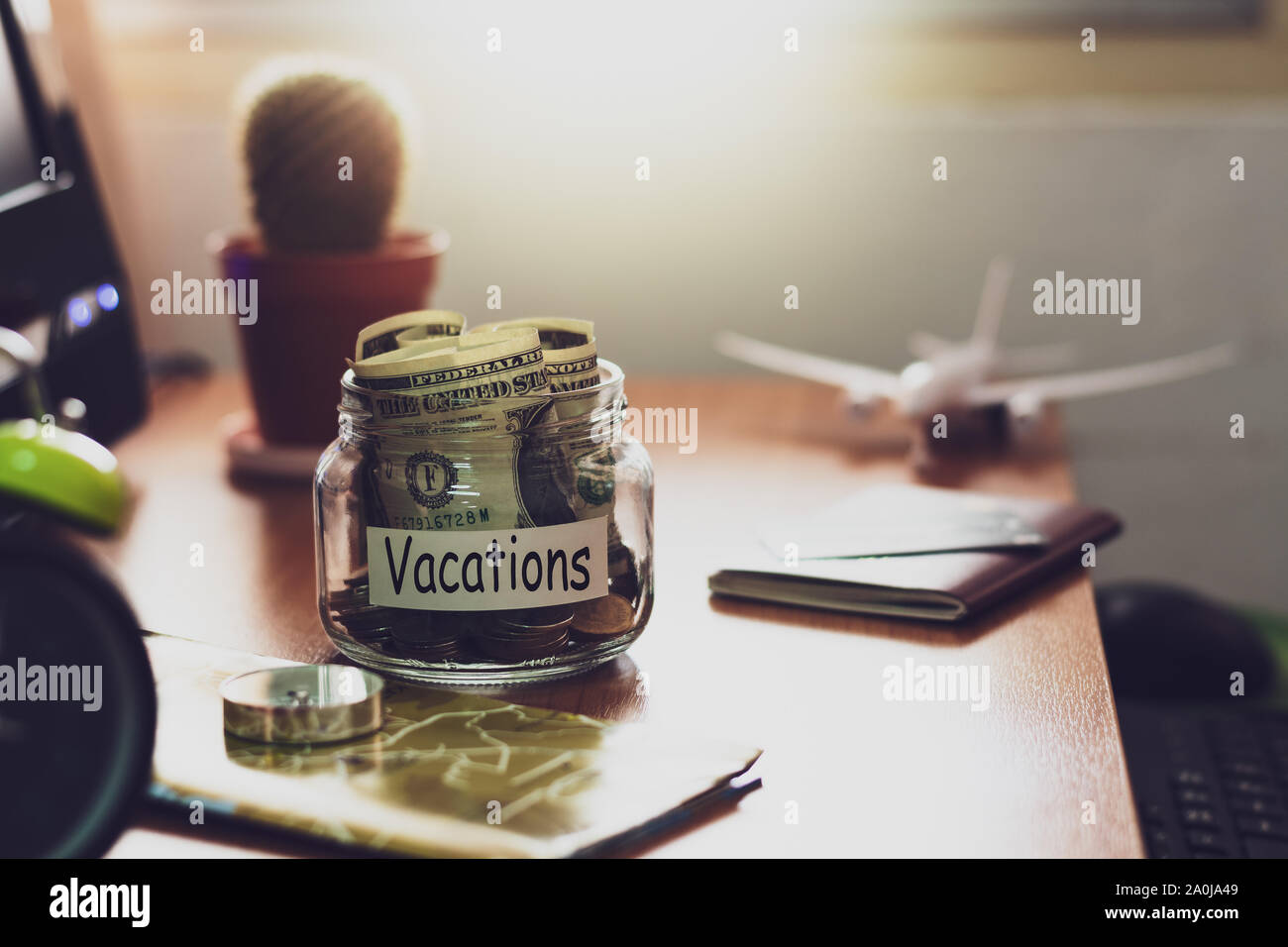 Vacanza il concetto di bilancio. Il denaro per le vacanze risparmi in un vasetto di vetro con la bussola, passaporto, orologio, carta di credito, aereo giocattolo e mappa del mondo del lavoro Foto Stock