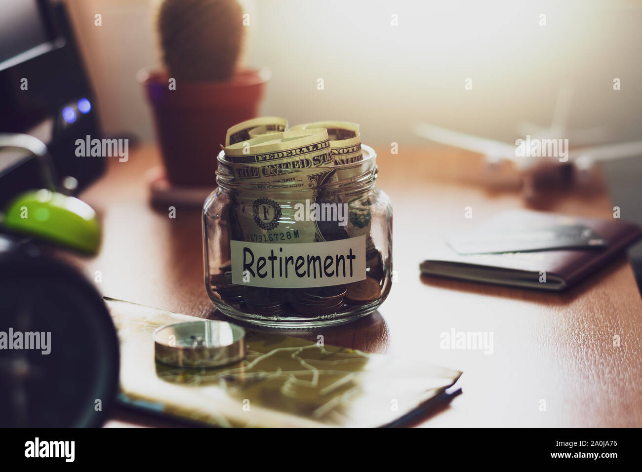 Bilancio di pensionamento concetto. I soldi per il risparmio pensionistico in un vasetto di vetro con la bussola, passaporto, orologio, carta di credito, aereo giocattolo e mappa del mondo sulla worki Foto Stock