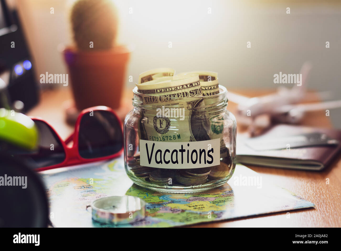 Vacanza il concetto di bilancio. Il denaro per le vacanze risparmi in un vasetto di vetro con la bussola, passaporto, occhiali da sole, carta di credito e di aeromobili toy sulla mappa del mondo Foto Stock