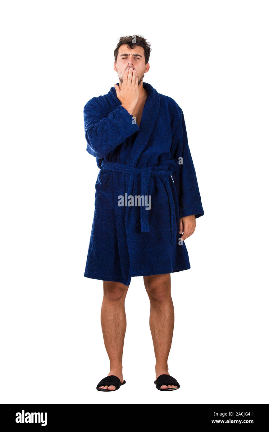 A piena lunghezza Ritratto di sleepy giovane disordinati capelli, indossa accappatoio blu sbadigli, che copre la bocca con la mano isolati su sfondo bianco. Foto Stock