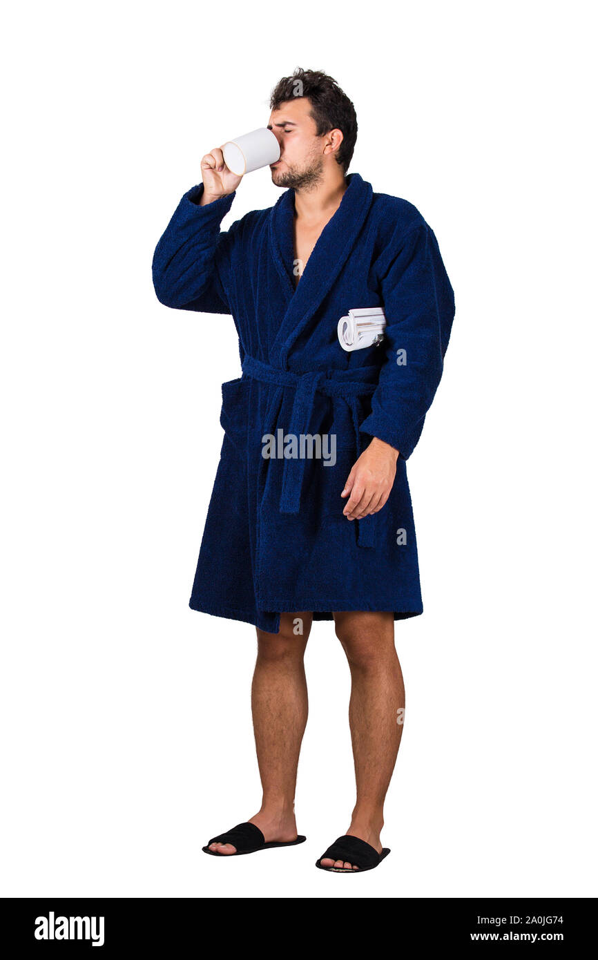 A piena lunghezza Ritratto di sleepy giovane disordinati capelli, indossa accappatoio blu e di bere il caffè dalla sua tazza come tenere un giornale del mattino in mano, isolare Foto Stock