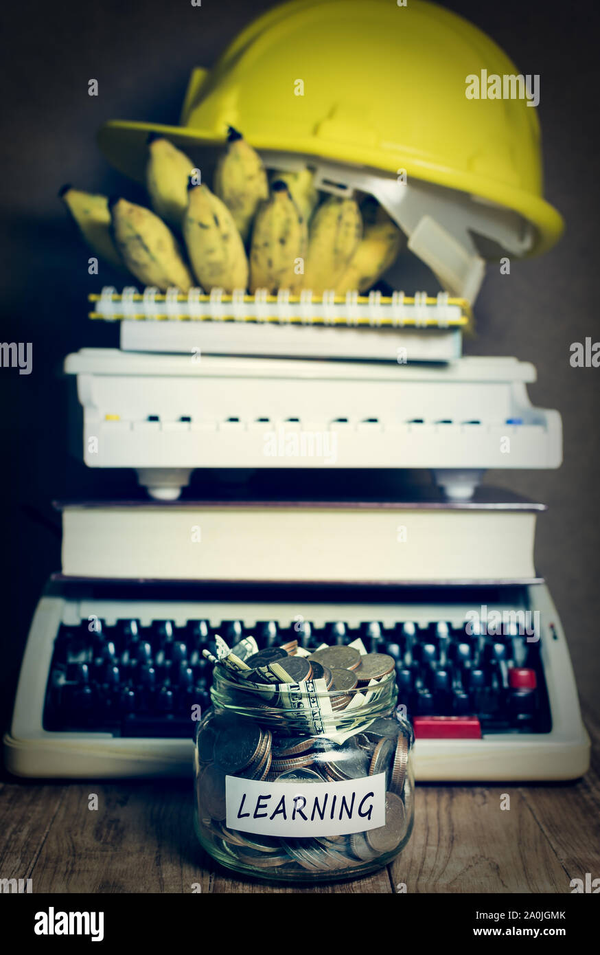 Risparmiare denaro per l'apprendimento in un barattolo di vetro con il mucchio di nastri inchiostratori per macchine da scrivere, libro di testo, pianoforte, notepad, banana e casco di costruzione Foto Stock