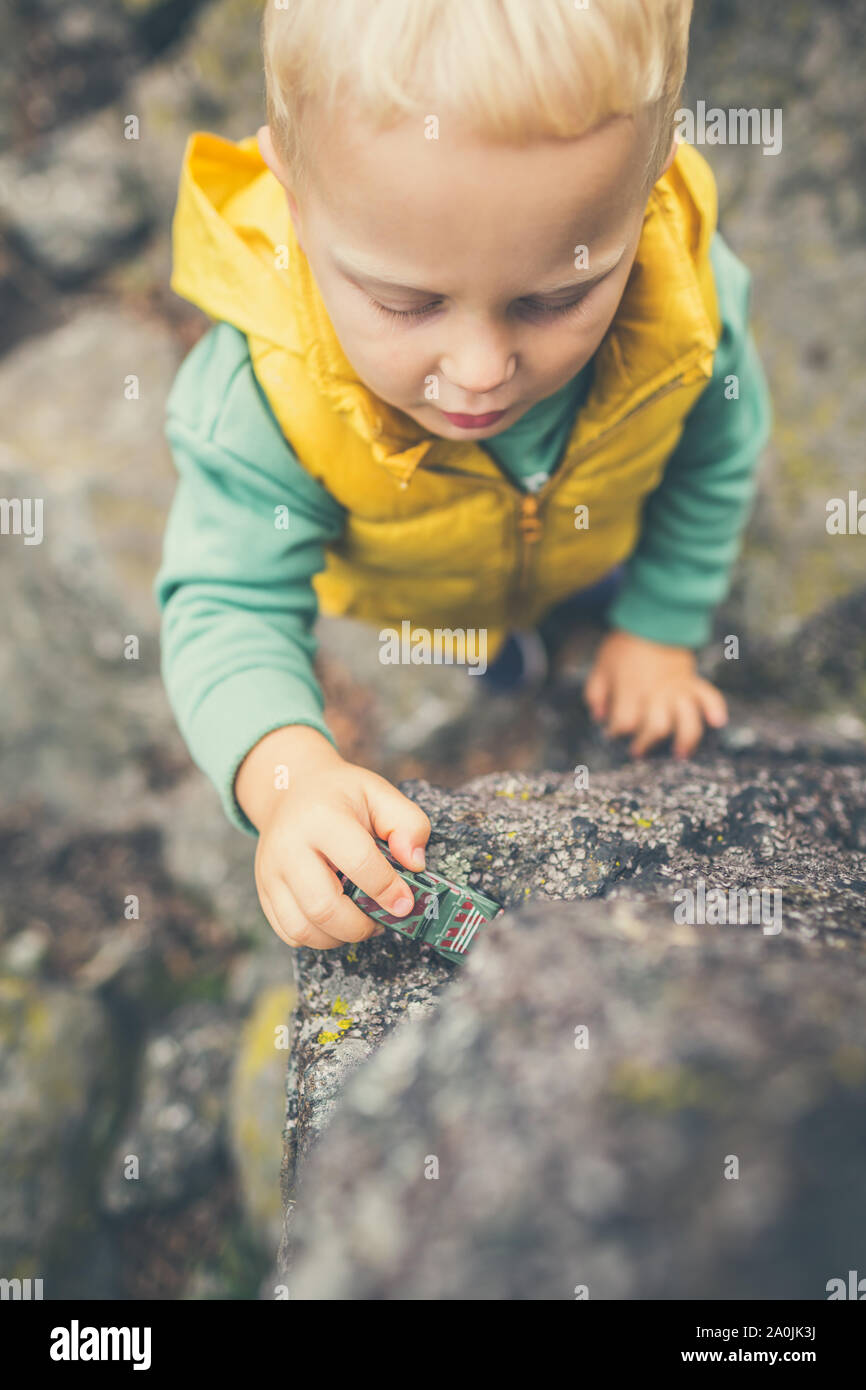 Il Toddler boy giocare con giocattoli su una roccia. Bambino passeggiate sulle montagne rocciose. Foto Stock