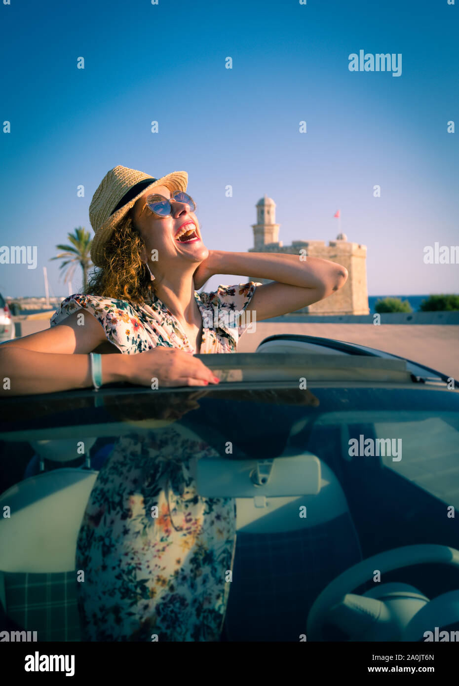 Donna sorridente con cappello di paglia e occhiali da sole godendo di estate in una vettura convertibile. mano saluto. Il concetto di strada viaggi e avventura. equitazione con Foto Stock