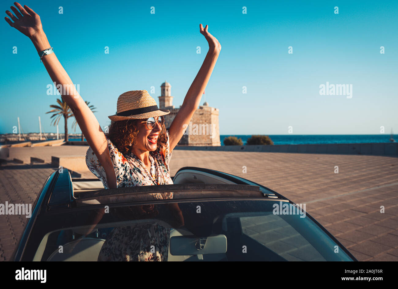 Donna sorridente con cappello di paglia e occhiali da sole godendo di estate in una vettura convertibile. mano saluto. Il concetto di strada viaggi e avventura. equitazione con Foto Stock