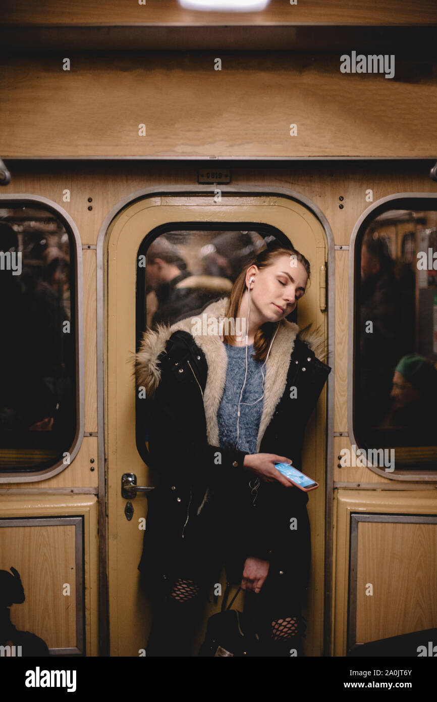 Giovane donna ascoltando musica su smart phone che viaggiano in treno della metropolitana Foto Stock