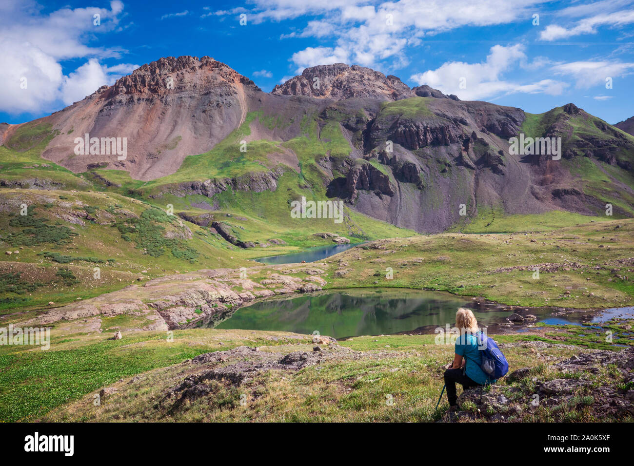 La donna si siede su una roccia ammirando laghetti alpini nel lago ghiacciato bacino superiore in San Juan National Forest, Silverton, Colorado, STATI UNITI D'AMERICA Foto Stock