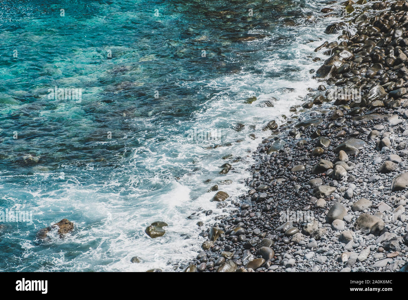 Le onde del mare sulla spiaggia di pietra con ciottoli neri a costa rocciosa - Foto Stock