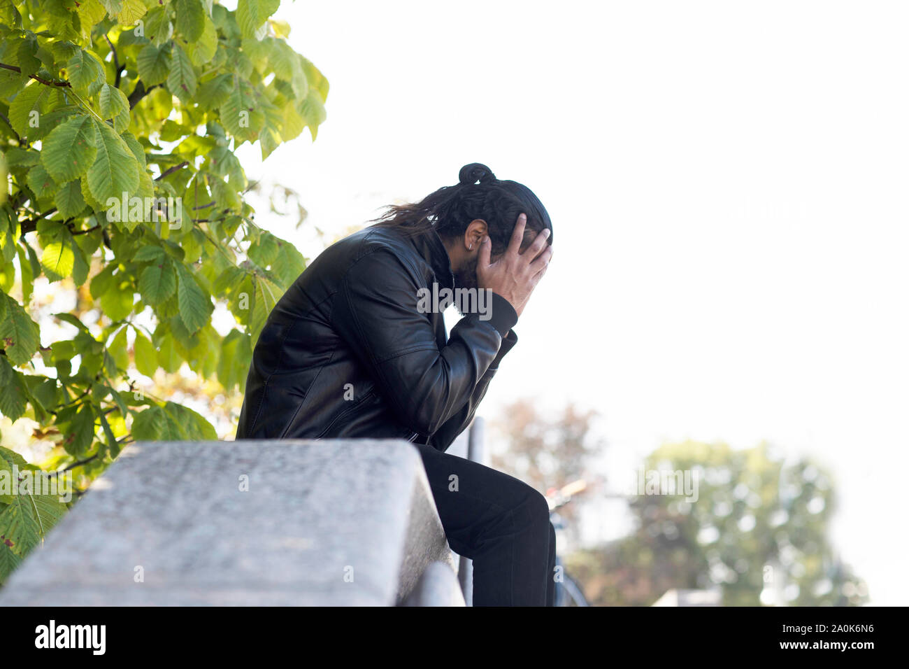 Giovane uomo seduto fuori e tenendo le mani prima di testa Foto Stock