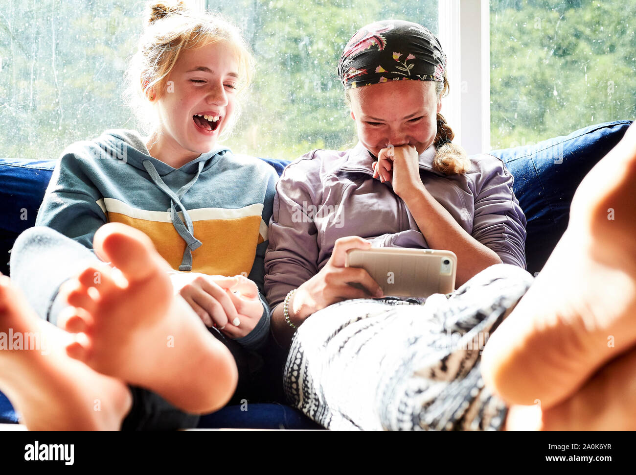 Teen ragazze ridere su un divano guardando qualcosa su un telefono Foto Stock