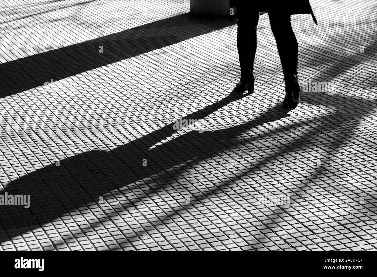 Silhouette sfocate ombra delle gambe di una donna in tacchi alti camminando sulle mattonelle passerella pedonale della città in inverno in alto contrasto bianco e nero Foto Stock