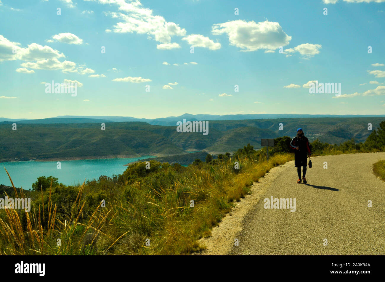 Uomo di fare escursioni con lo sport vestiti e una macchina fotografica in mano accanto ad un serbatoio di acqua in una montagna con un cielo blu e nuvole bianche Foto Stock
