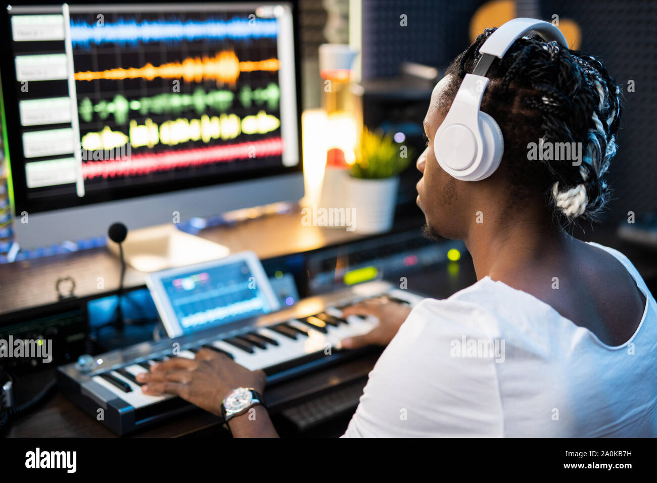 Giovane musicista nelle cuffie guardando le forme d'onda audio sullo schermo del computer Foto Stock