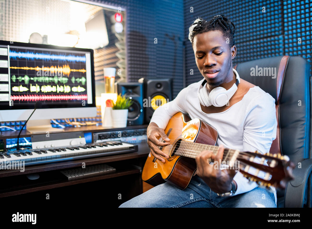 Contemporary giovane musicista o il chitarrista in informale a suonare la chitarra in studio Foto Stock