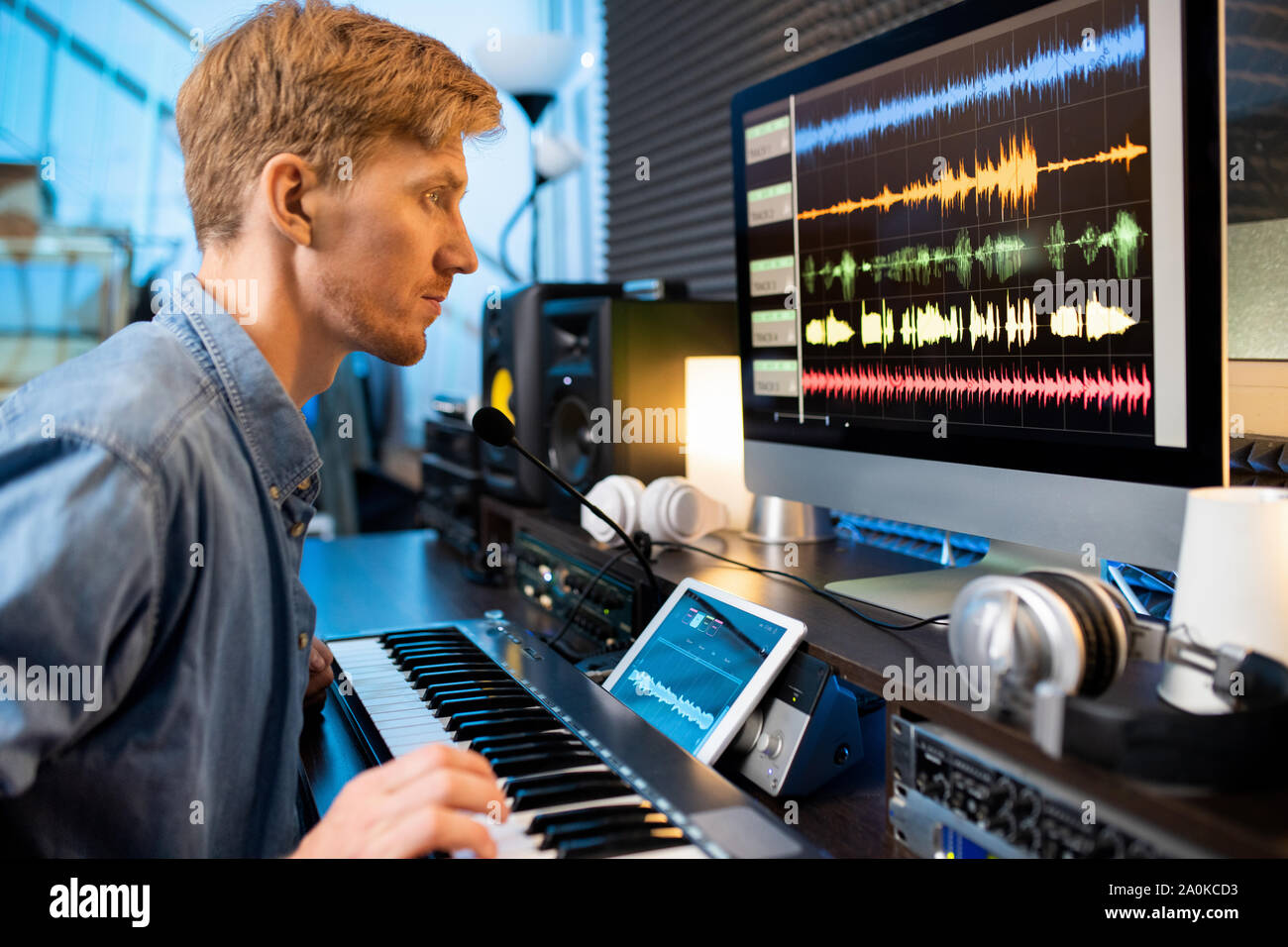 Uomo serio toccare uno dei tasti pianoboard mentre guardando le forme d'onda audio Foto Stock