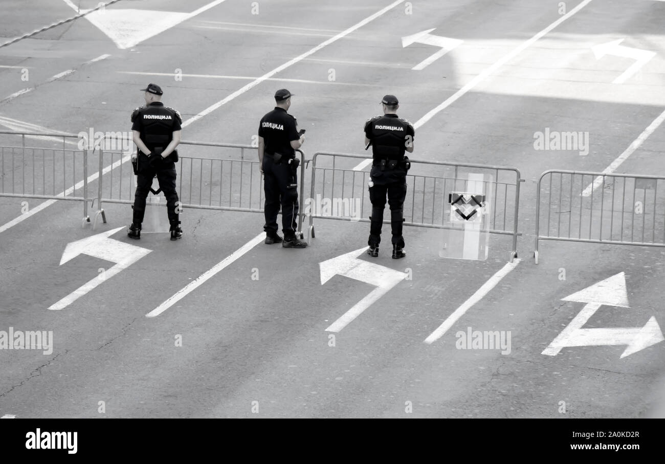 Belgrado, Serbia - 15 Settembre 2019: tre poliziotti di fronte temporanea recinzione barricade sulla strada di città, da dietro in bianco e nero Foto Stock