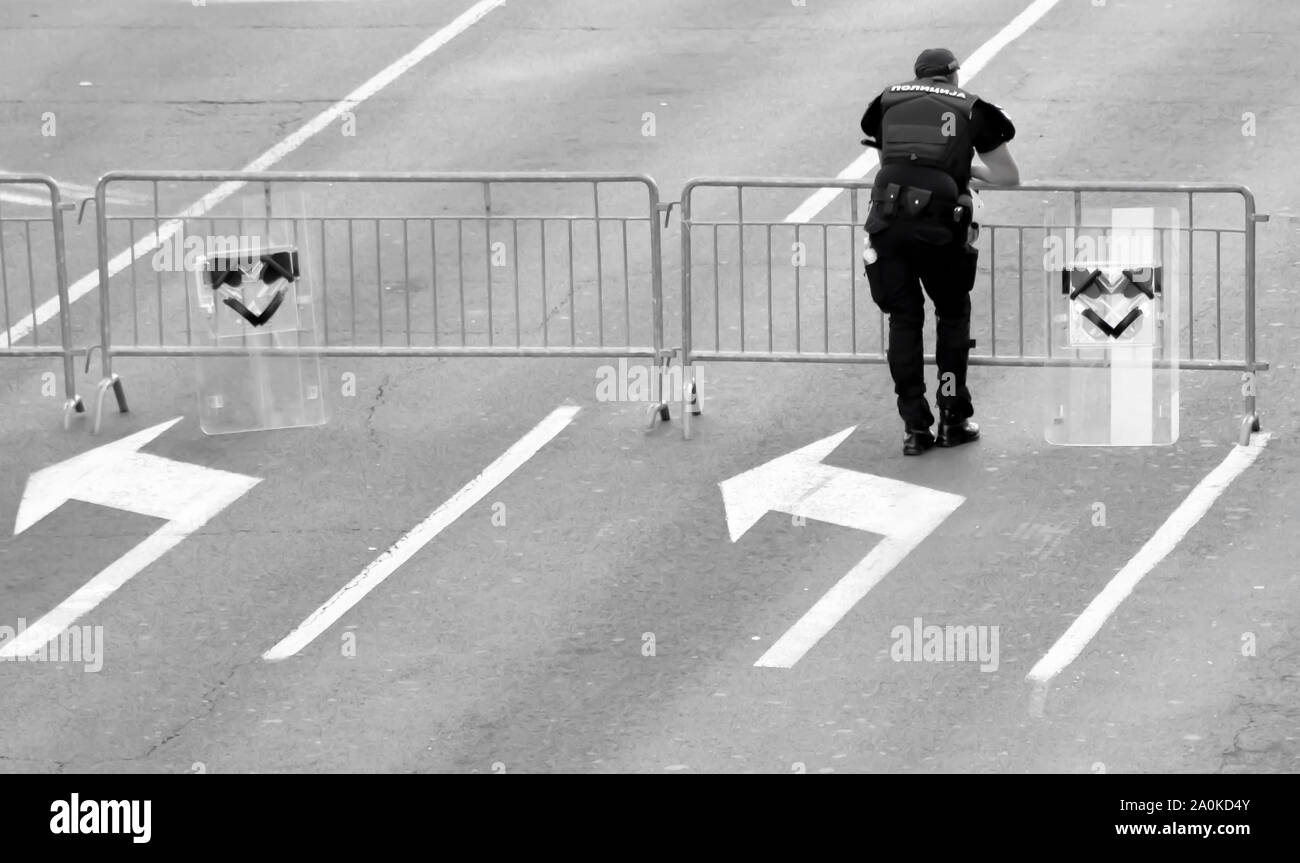 Belgrado, Serbia - 15 Settembre 2019: un poliziotto e due scudi appoggiati sulla temporanea barricade recinto sulla strada di città, da dietro in nero e bianco Foto Stock