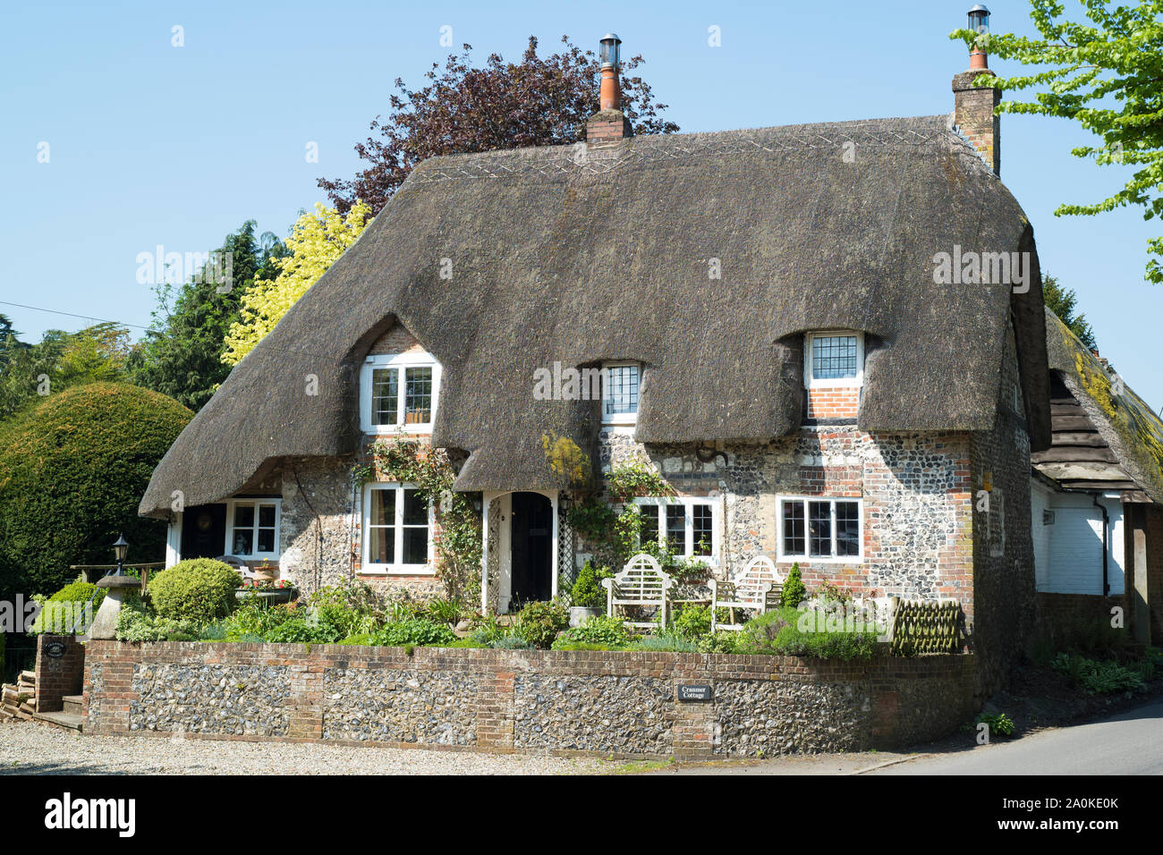Inglese tipica pietra costruito cottage con tetto in paglia in mattoni e pietra focaia costruzione tetto, ricoprendo di paglia, camini in Ramsbury, Wiltshire, Regno Unito Foto Stock