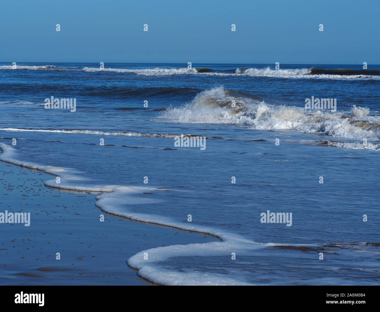 Le onde che si infrangono con white surf ed un cielo blu chiaro a Mablethorpe, Lincolnshire, Inghilterra Foto Stock