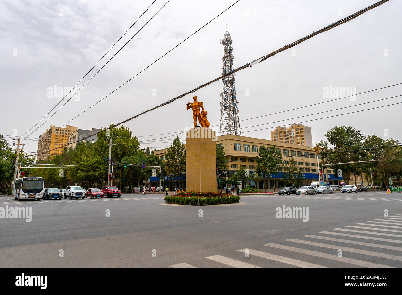 Hotan occupato Ring Road centrato con la statua di bronzo di un contadino uigura con un cappello tenendo una pala e vestiti Foto Stock
