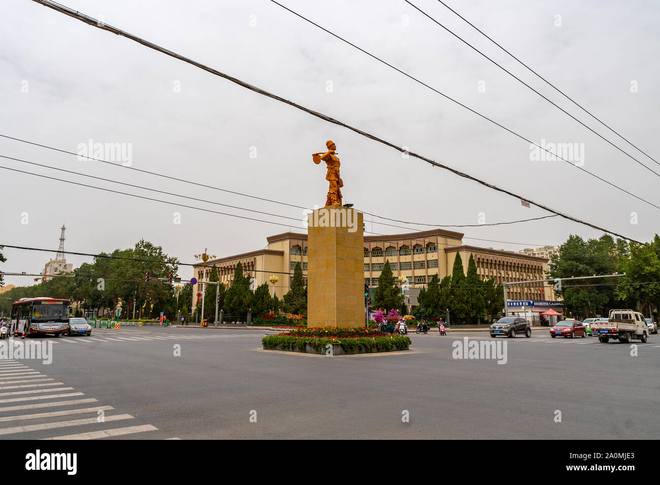 Hotan occupato Ring Road centrato con la statua di bronzo di un contadino uigura con un cappello tenendo una pala e vestiti Foto Stock