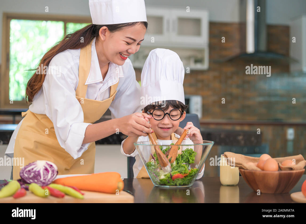 Felice bella donna asiatica e carino piccolo ragazzo con occhiali preparare per la cottura nella cucina di casa. La gente di stili di vita e famiglia. Cibo fatto in casa e Foto Stock