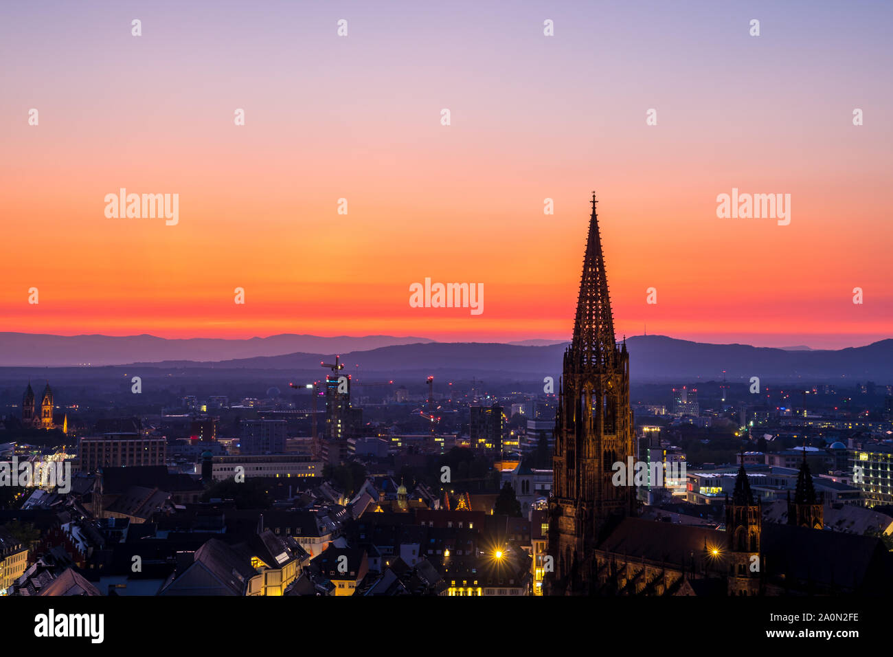 Germania, intensivi cielo rosso del tramonto su muenster chiesa steeple e sullo skyline della città di Freiburg im Breisgau in estate circondato dalla foresta nera Foto Stock