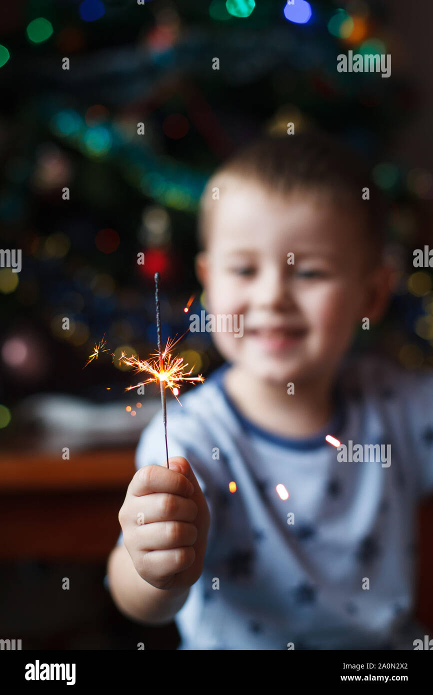 Splendido piccolo bambino holding burning sparkler per la Vigilia di Capodanno, bengala fire. Selezionare la messa a fuoco sui fuochi d'artificio. Foto Stock
