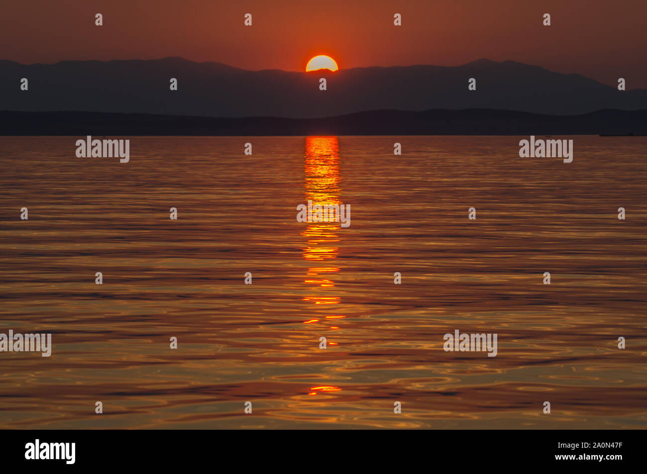 Il sole affonda dietro le colline sulla costa dell'Istria. Il mare è a riflettere la sua luce. Foto Stock