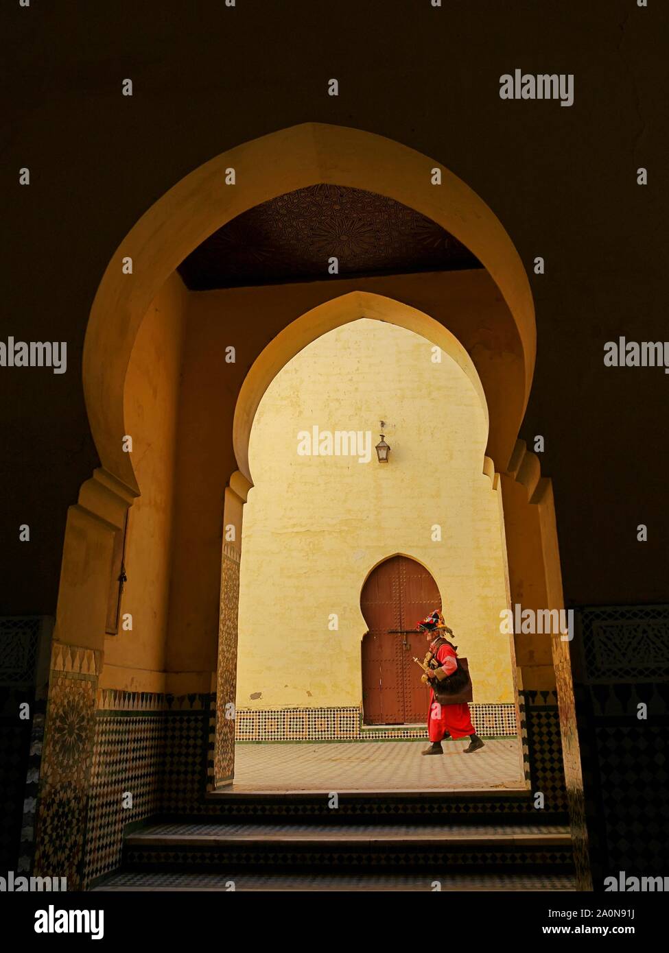 Un vettore acqua o 'guerrab' nel colorato costume tradizionale visto attraverso gli archi di Moulay Ismail palace, Meknes, Marocco Foto Stock