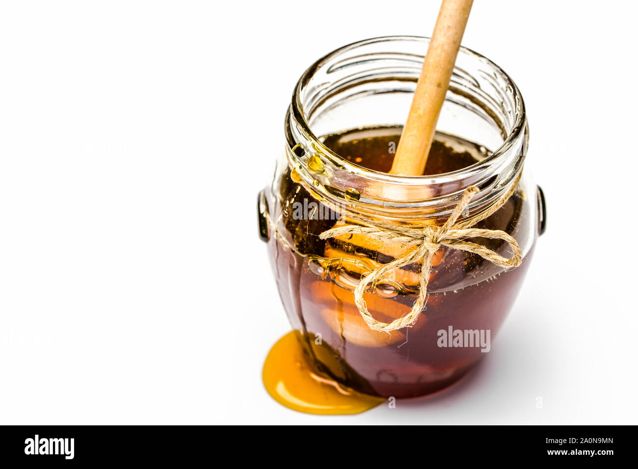 Il gocciolamento di miele e stick immerso nel vaso di vetro di miele su sfondo bianco Foto Stock