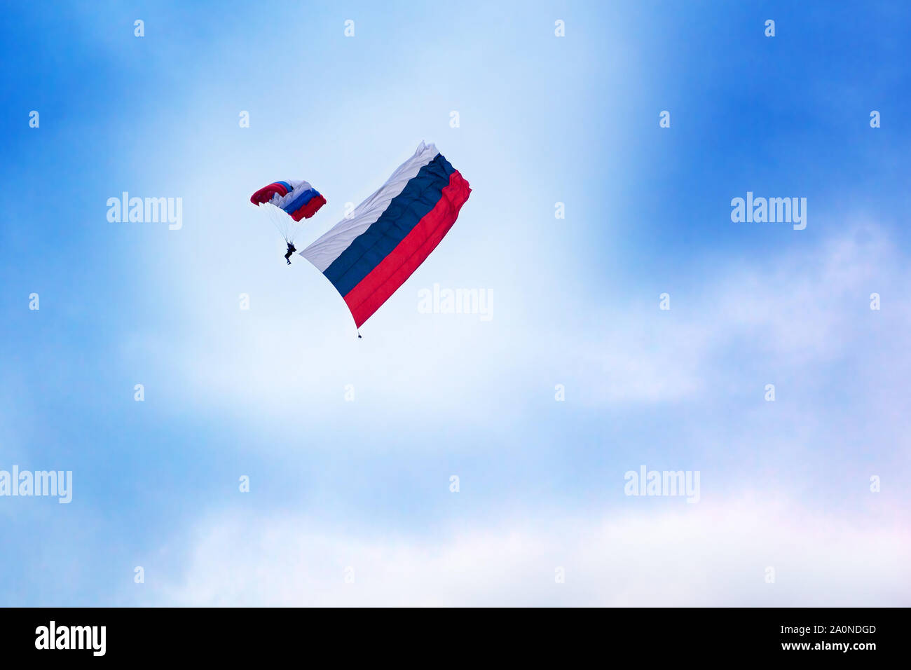 Paracadutista russa salta con un paracadute verniciato nei colori della bandiera della Russia con la bandiera russa su chiaro cielo blu e nuvole bianche indietro Foto Stock