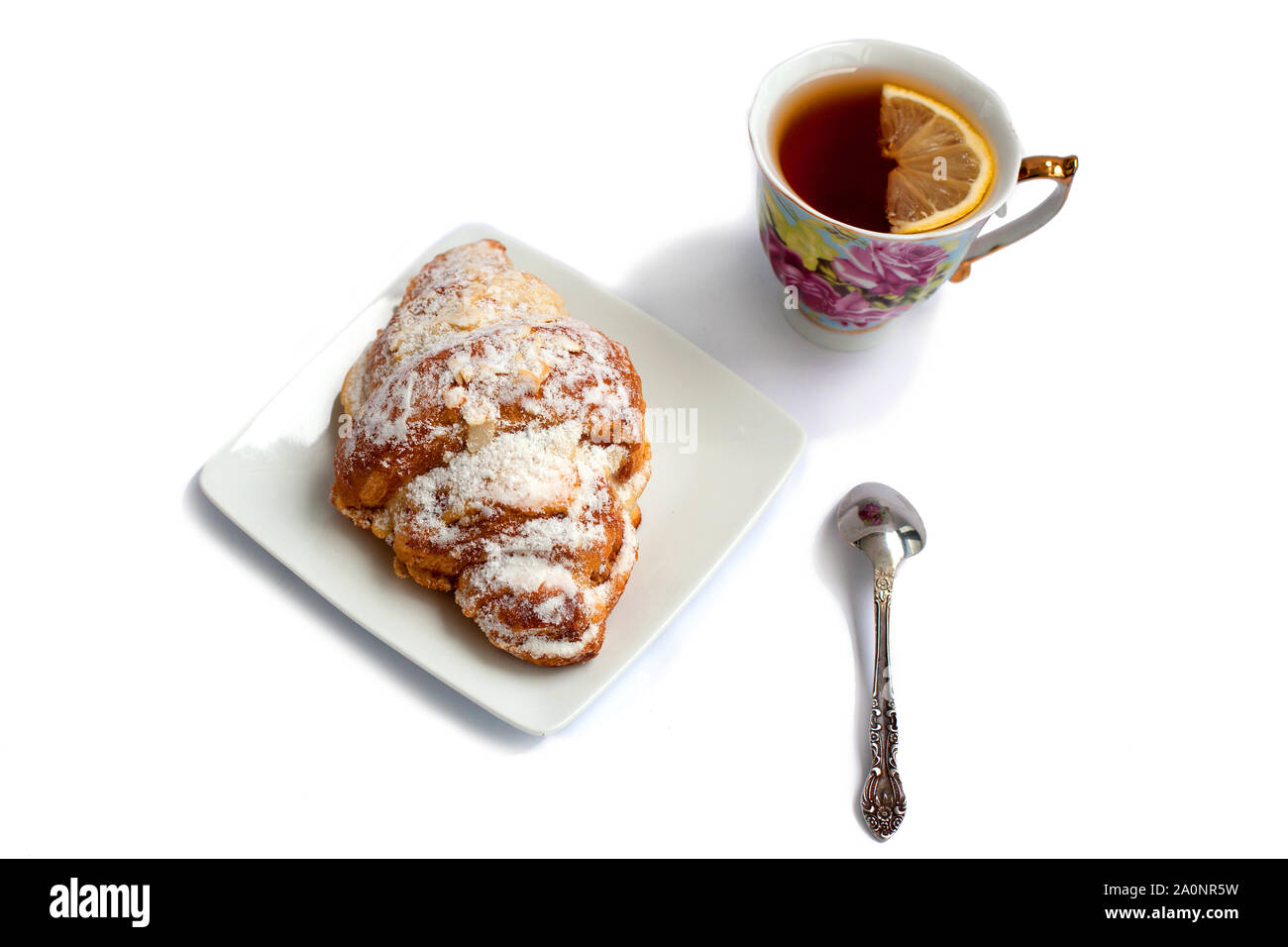 Croissant su una piastra bianca con una tazza di tè con limone e un cucchiaio su sfondo bianco Foto Stock