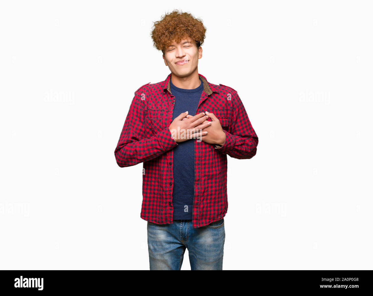 Giovane studente bello uomo con capelli Afro indossa una camicia sorridente con le mani sul petto con gli occhi chiusi e grato gesto sul viso. Concetto di salute. Foto Stock