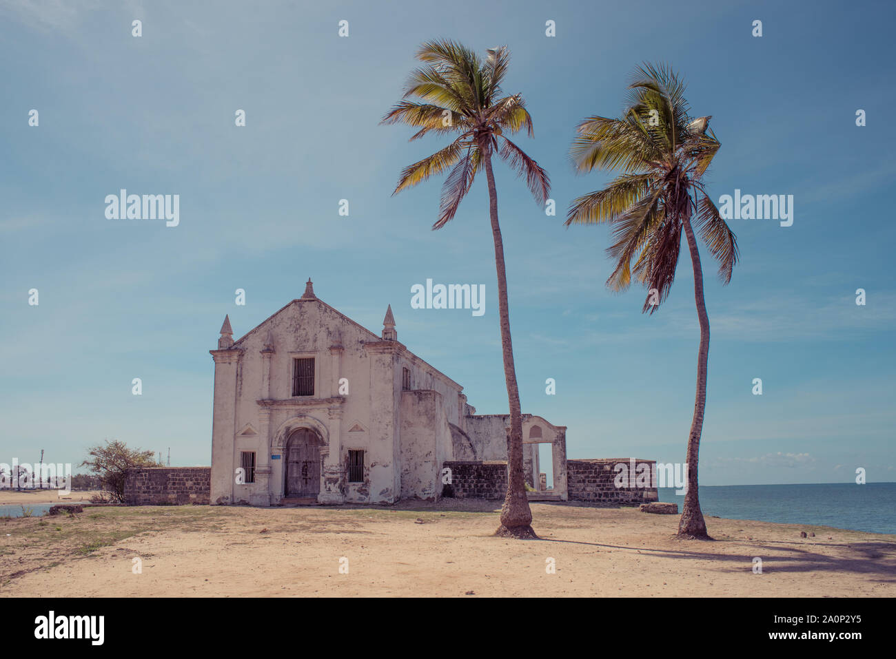 Un vecchio weathered bianco lavato chiesa sulla spiaggia dell'isola di Mozambico (Ilha de Mocambique), con due alberi di palma in primo piano. Nampula Pro Foto Stock