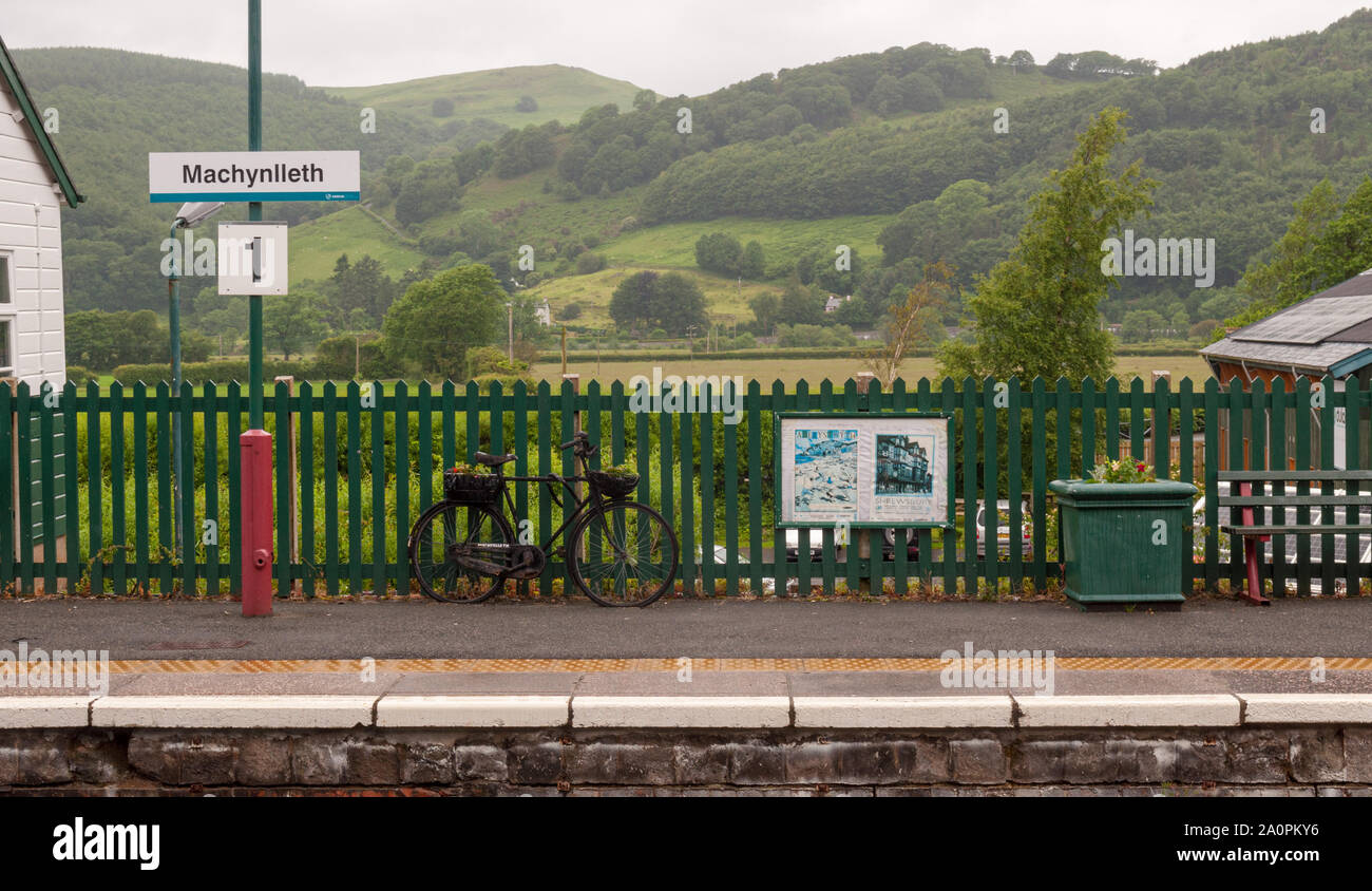 Machynlleth, Wales, Regno Unito - 21 Giugno 2012: colline boscose del mid-Wales salire dietro la piattaforma della stazione di Machynlleth. Foto Stock