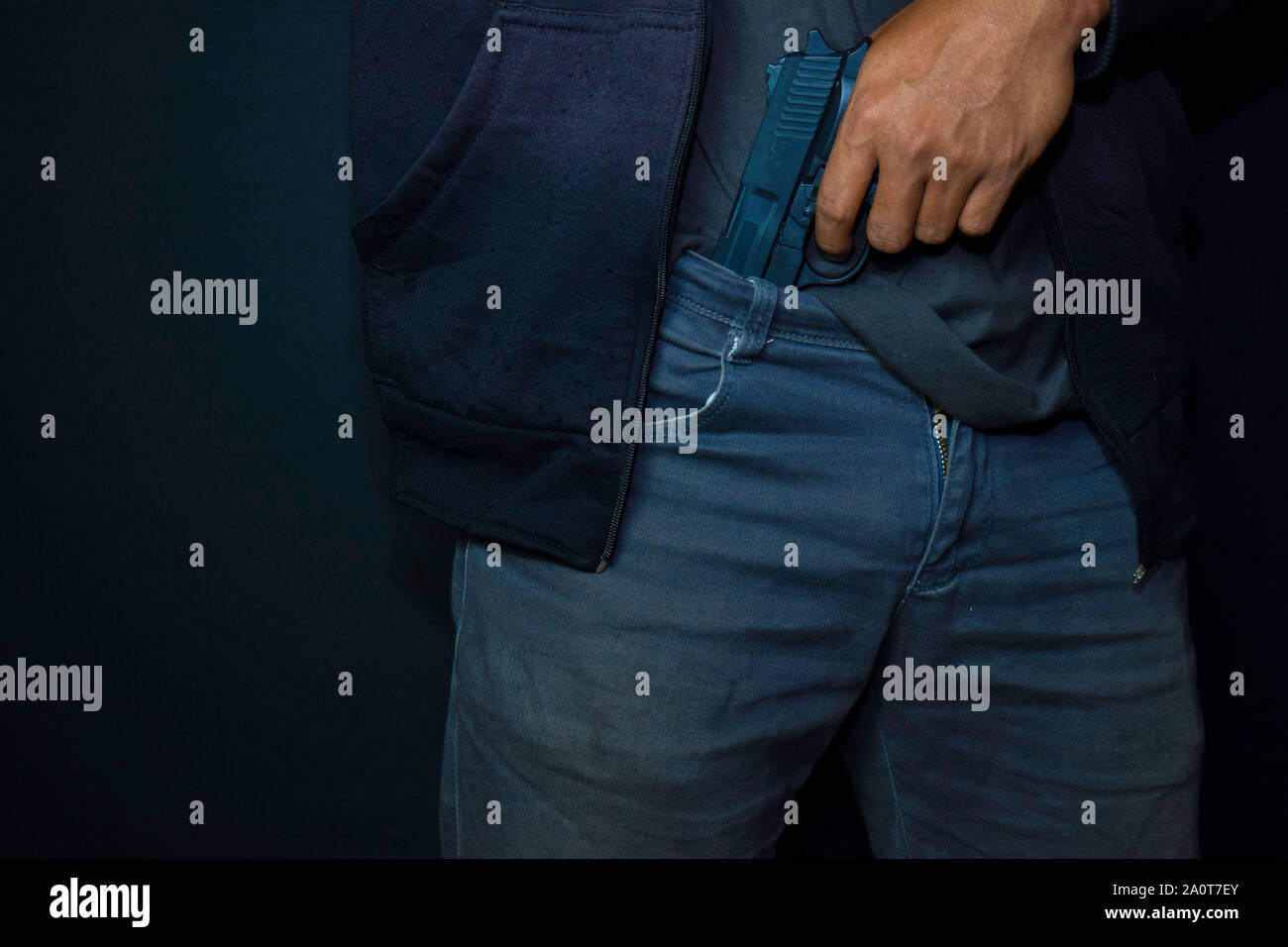 Uomo asiatico detiene una pistola. Pistola nella sua pantaloni isolati su sfondo nero. Foto Stock