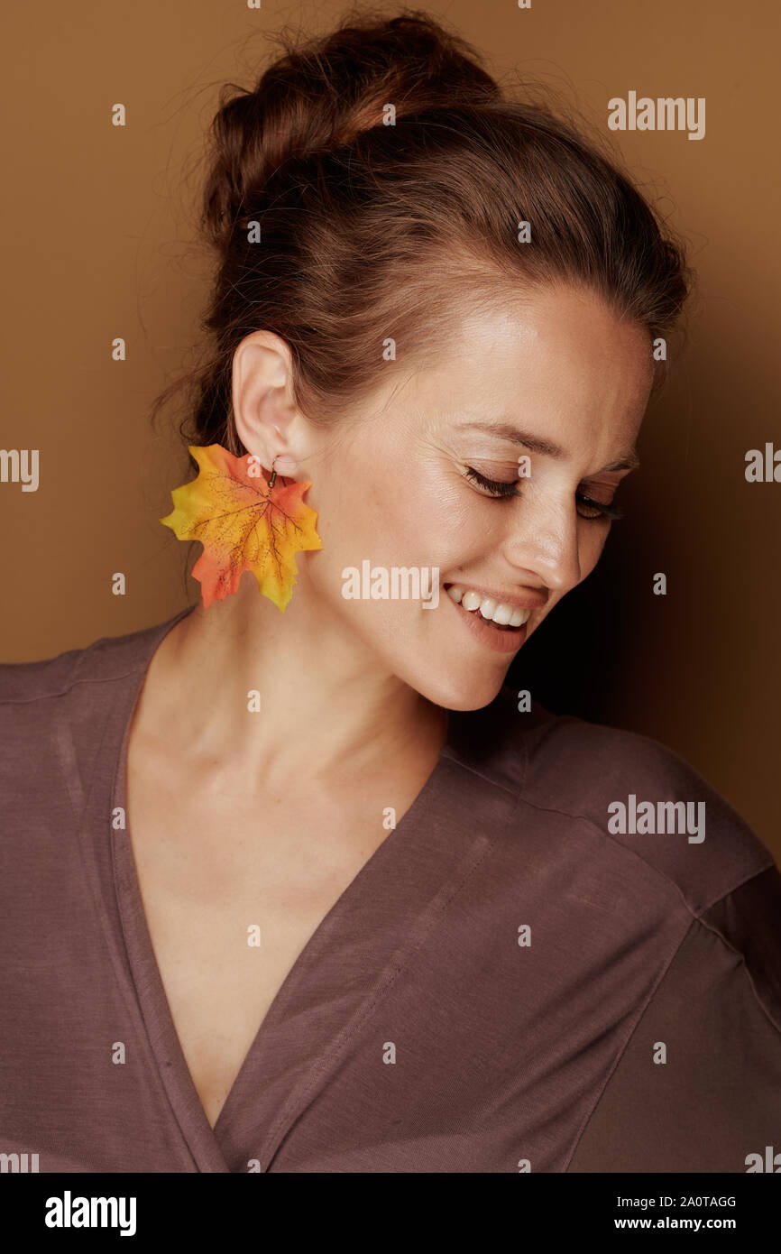 Ciao autunno. sorridente giovane donna in un accappatoio con foglie di autunno orecchini isolato sul beige. Foto Stock