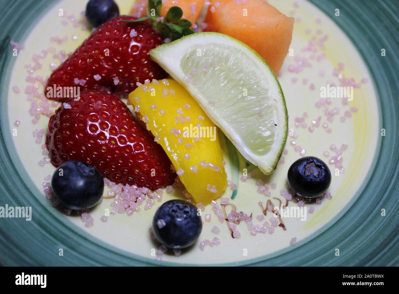 Close-up di limone tritata, fragola, mirtillo, mellon, avocado e papaya sulla piastra verde con lo zucchero sulla sommità di esso per dieta eccellente Foto Stock