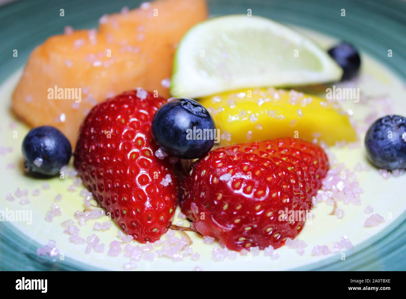 Close-up di limone tritata, fragola, mirtillo, mellon, avocado e papaya sulla piastra verde con lo zucchero sulla sommità di esso per dieta eccellente Foto Stock