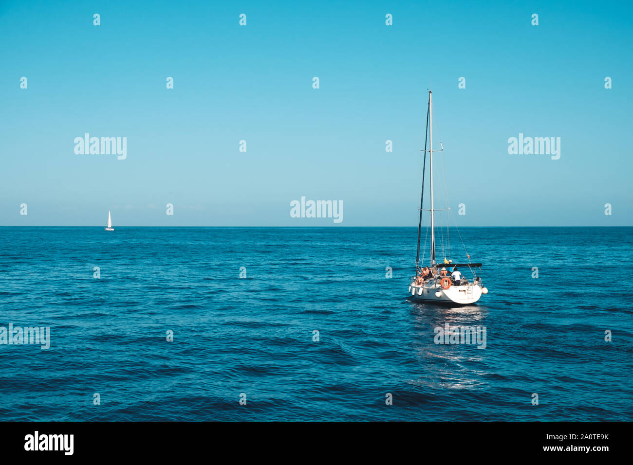 Imbarcazione a vela con un gruppo di persone sulla calma oceano su giornata soleggiata con cielo blu chiaro Foto Stock