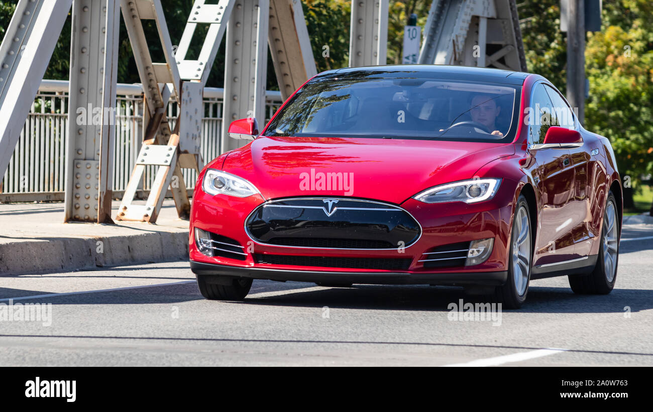 Uomo alla guida di Tesla Model S attraverso un ponte in una giornata di sole a Londra, Ontario. Foto Stock