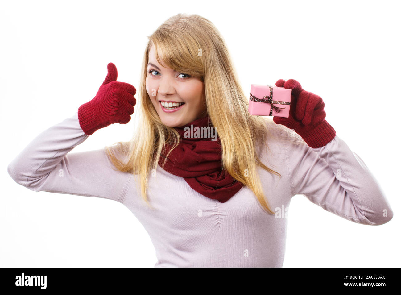 Donna sorridente in guanti holding avvolto regalo per Natale o altra celebrazione e mostrando pollice su sfondo bianco Foto Stock
