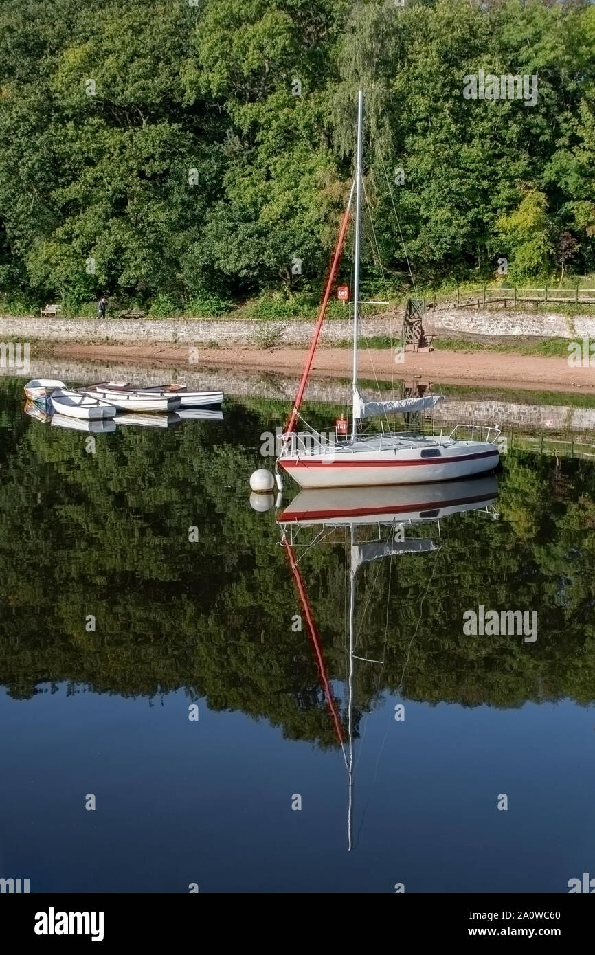 Una sola barca a vela sul lago con riflessi nell'acqua. Ormeggiate e con  tre piccole barche a remi ormeggiate anche dietro Foto stock - Alamy