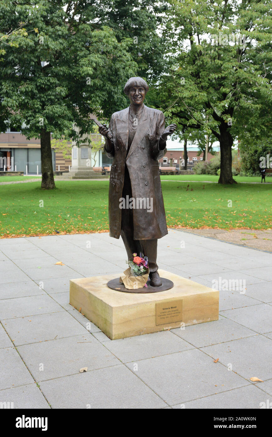 Statua di bronzo di Victoria Wood su zoccolo di pietra in zona lastricata in giardini biblioteca con alberi sullo sfondo in Bury lancashire uk Foto Stock