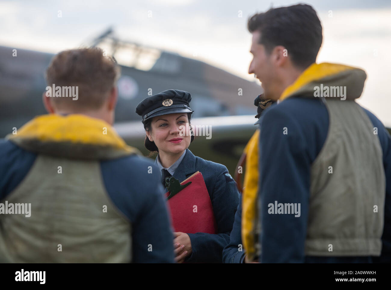 Membri della rievocazione storica lo spirito di gruppo della Gran Bretagna a piedi passato un Supermarine Spitfire sul flightline durante il Duxford Battle of Britain Air Show all'Imperial War Museum di Duxford, Cambridgeshire. Foto Stock