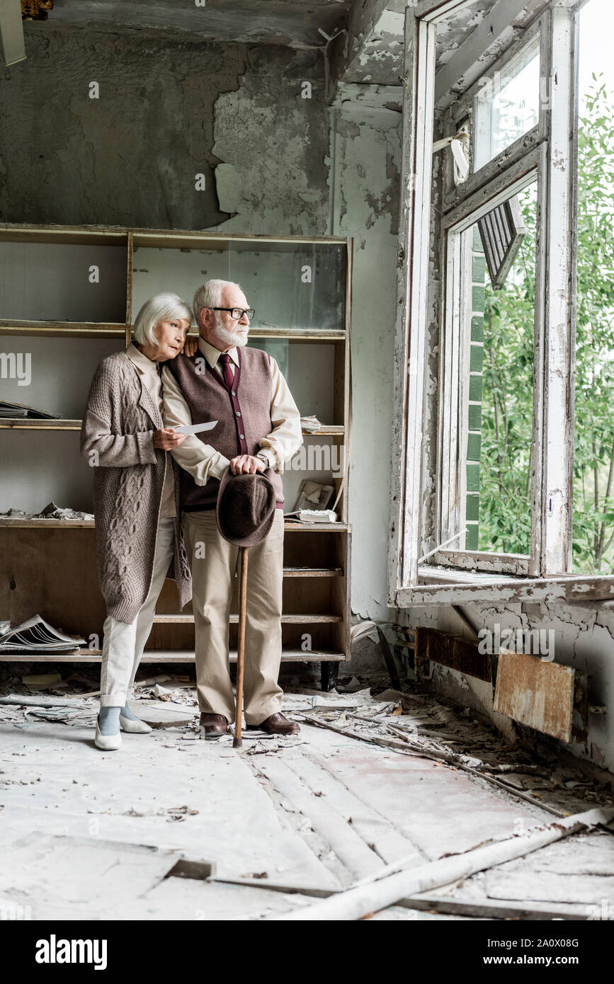 Coppia in pensione guardando alla finestra mentre in piedi in aula danneggiata Foto Stock