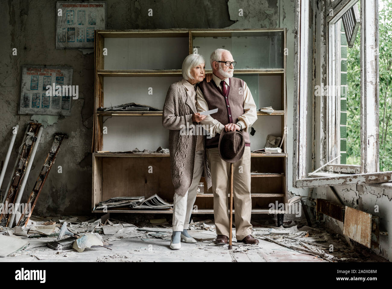 Ritirato l uomo e la donna che guarda la finestra mentre in piedi in aula danneggiata Foto Stock