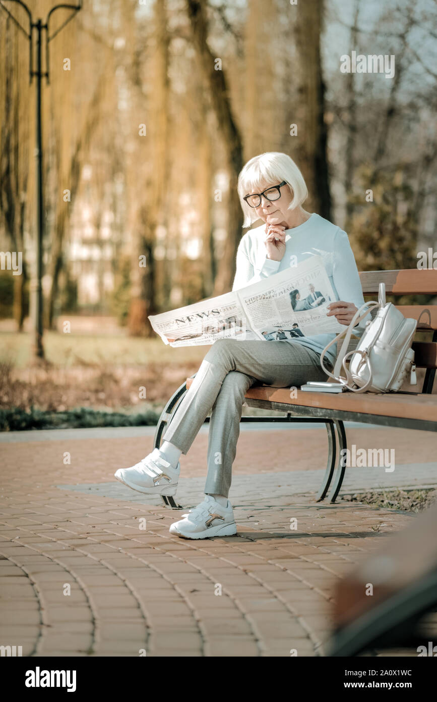 Piacevole antiquata lady in bicchieri minuziosamente quotidiano di lettura sul banco di lavoro Foto Stock